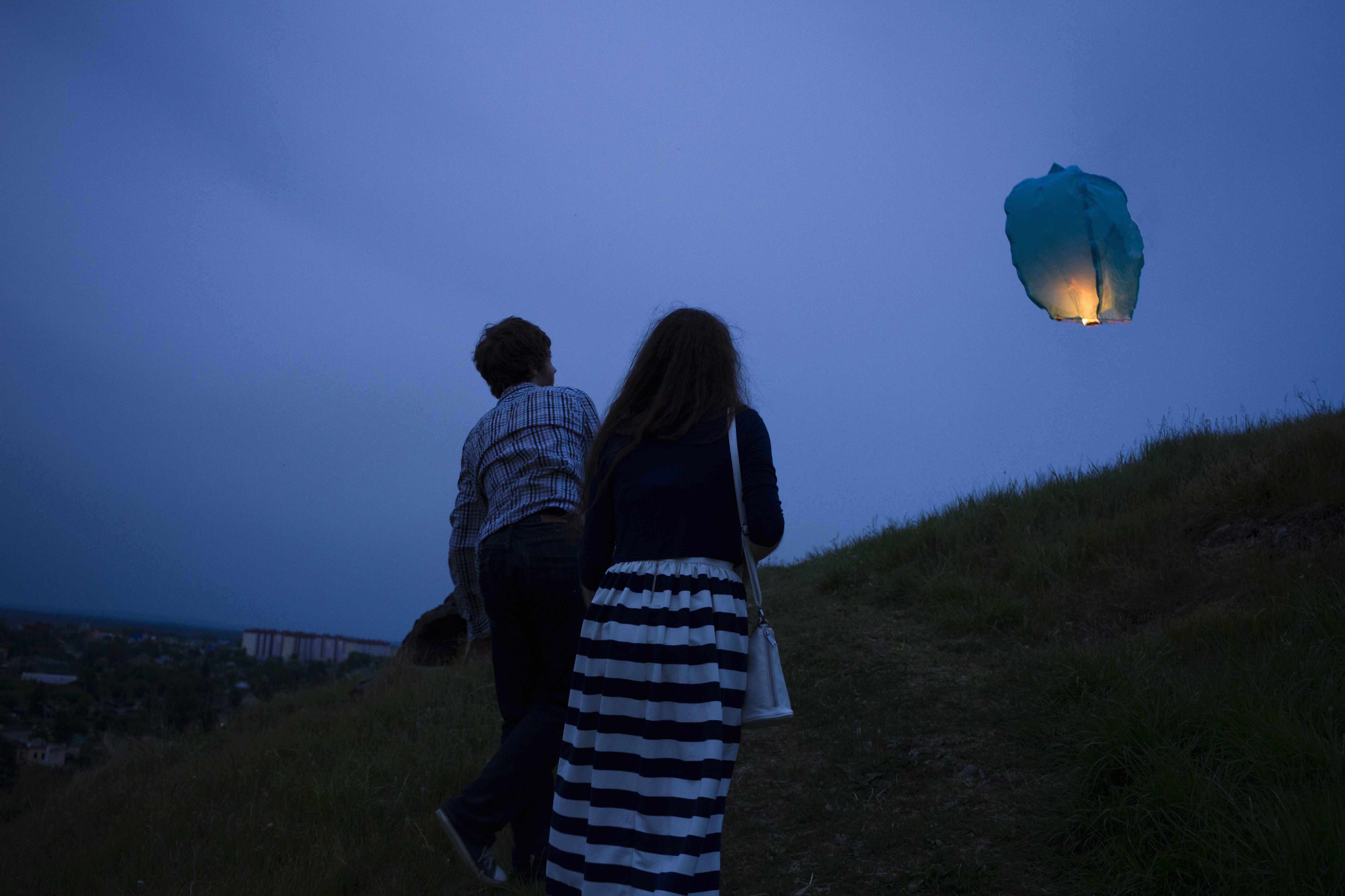 Couple walking up grassy hill at dusk, watching sky lantern in air. | Source: Getty Images