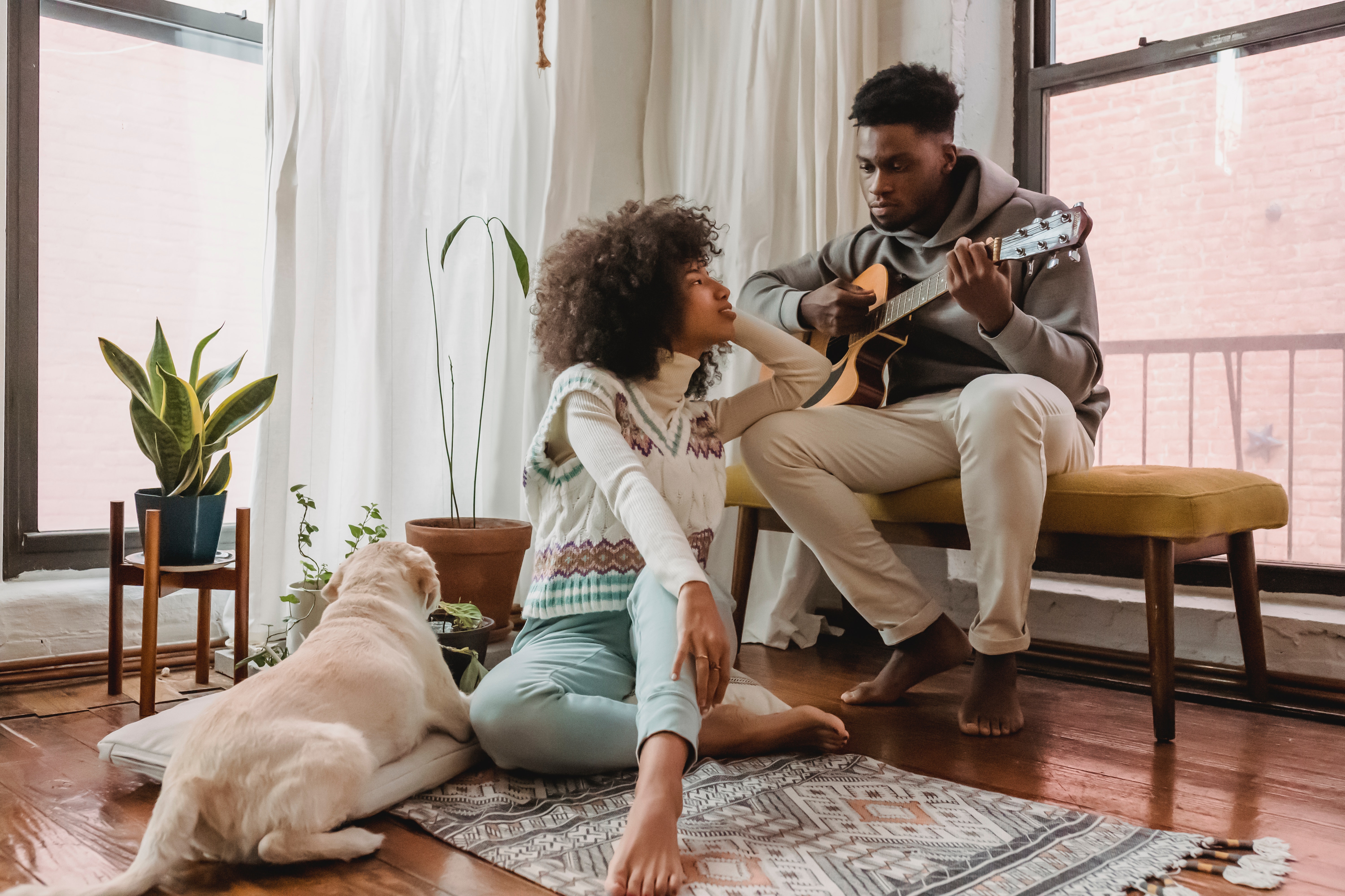 A man playing guitar while a woman sits on the floor. | Source: Pexels