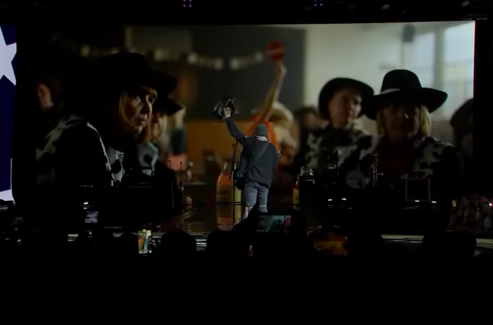 Billy Ray Cyrus turning away from the audience to watch the music video. | Source: YouTube/PBS NewsHour