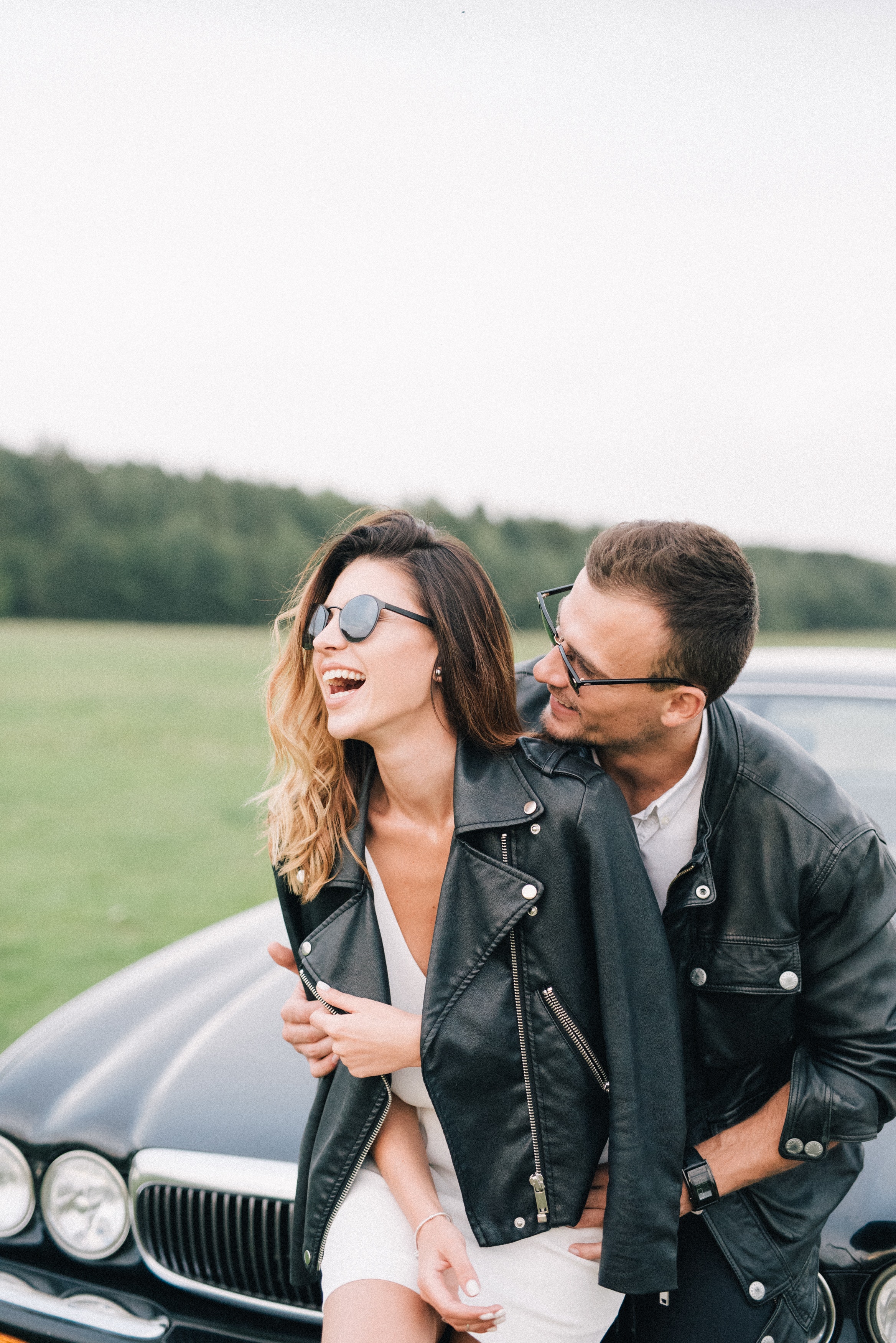A couple sits happily on the front hood of the car. | Source: Pexels