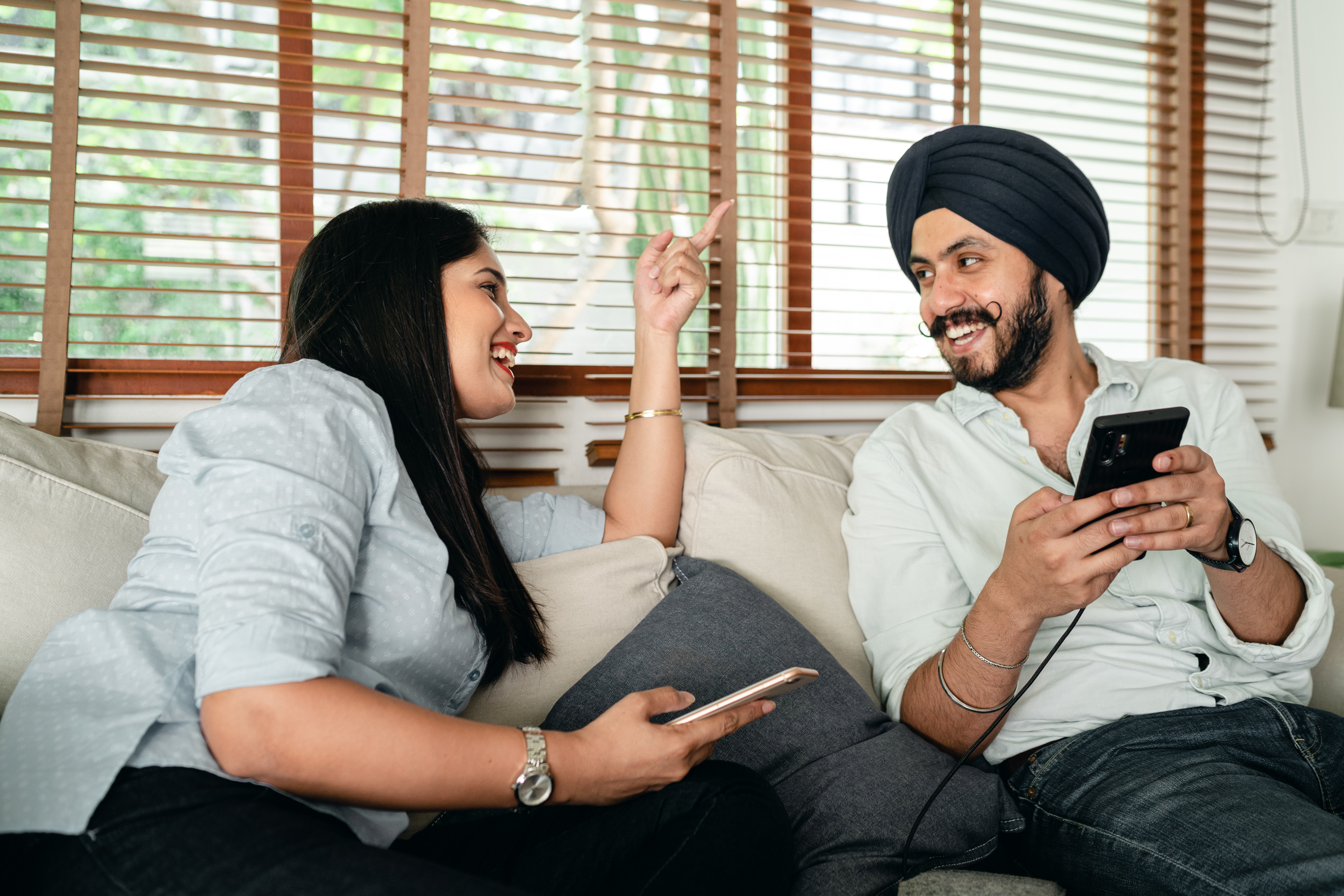 Happy Indian couple with mobile phones having fun on couch. | Source: Pexels