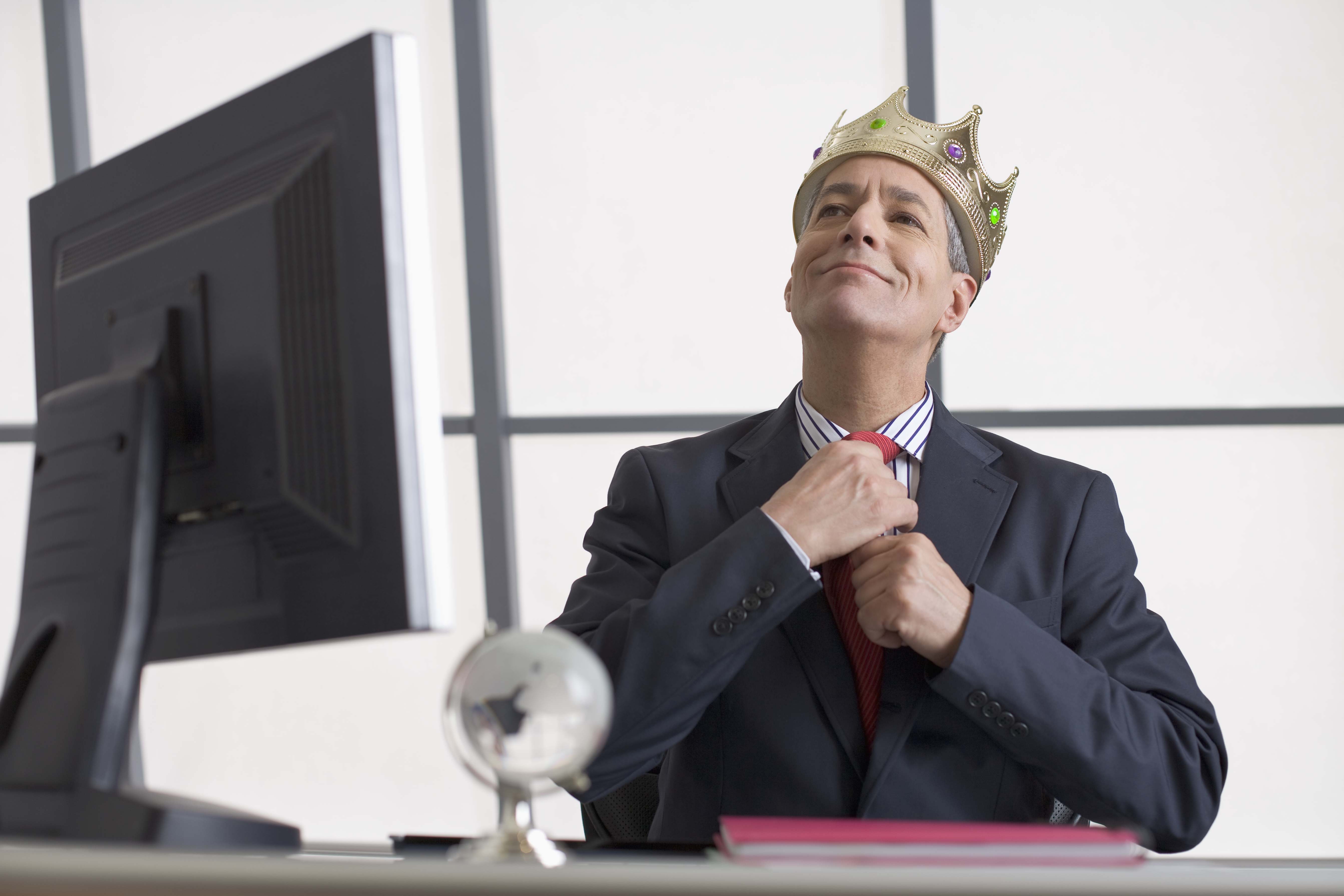 A man with crown fixing his tie while sitting at his desk. | Source: Getty Images