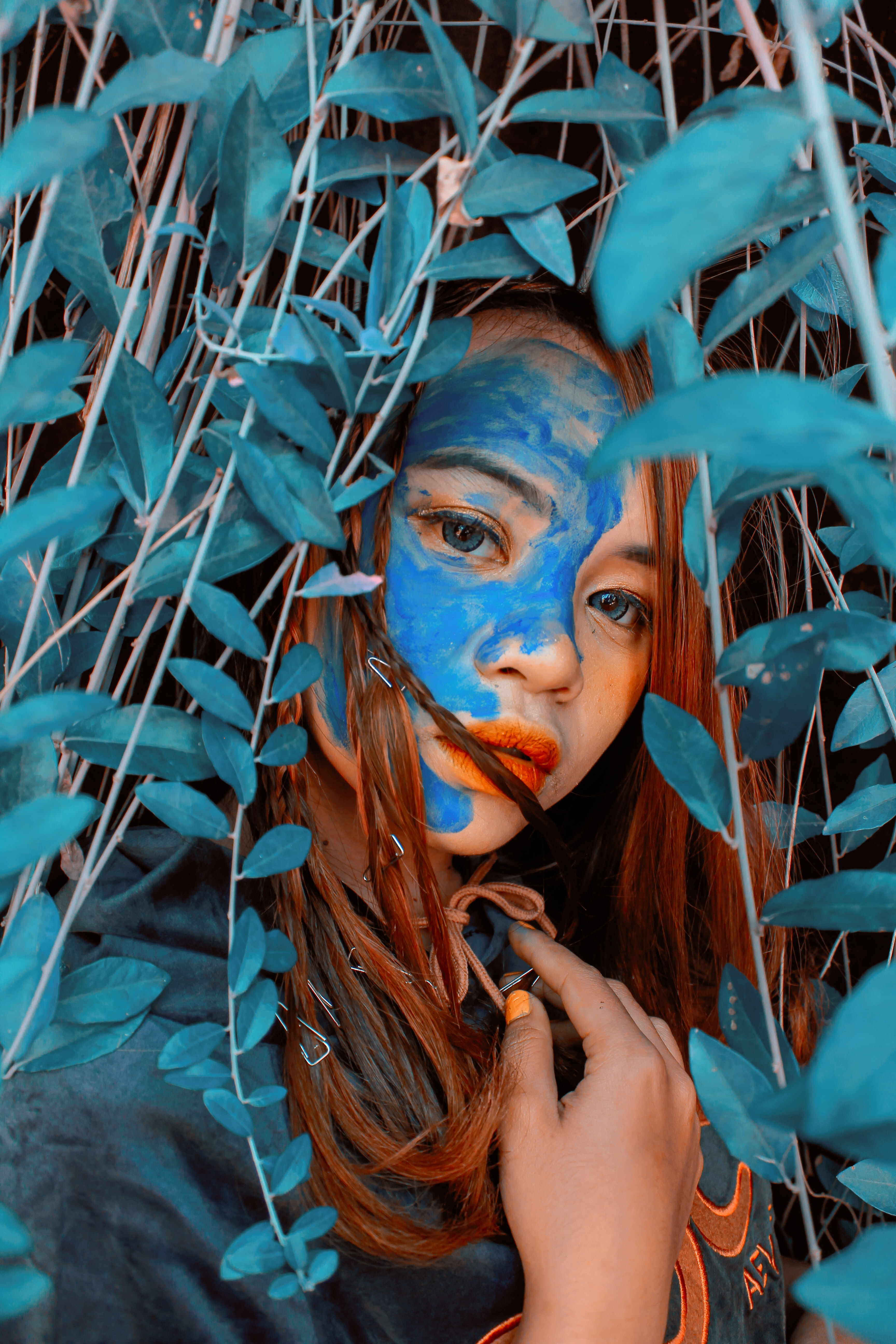 A woman with blue paint hiding within leaves. | Source: Pexels