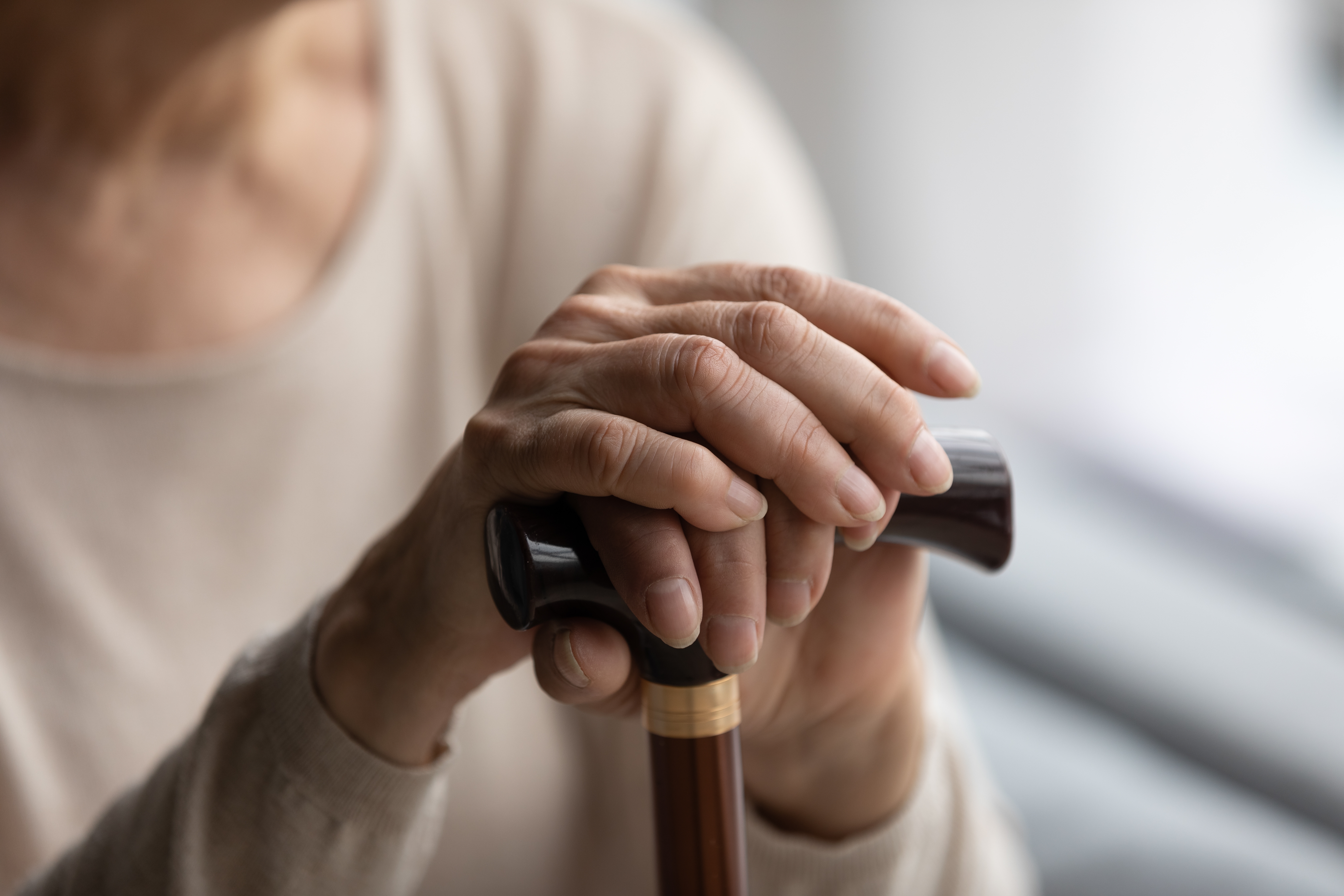 Primer plano enfocado de unas manos femeninas plegadas y arrugadas sobre un bastón de madera. | Fuente: Shutterstock