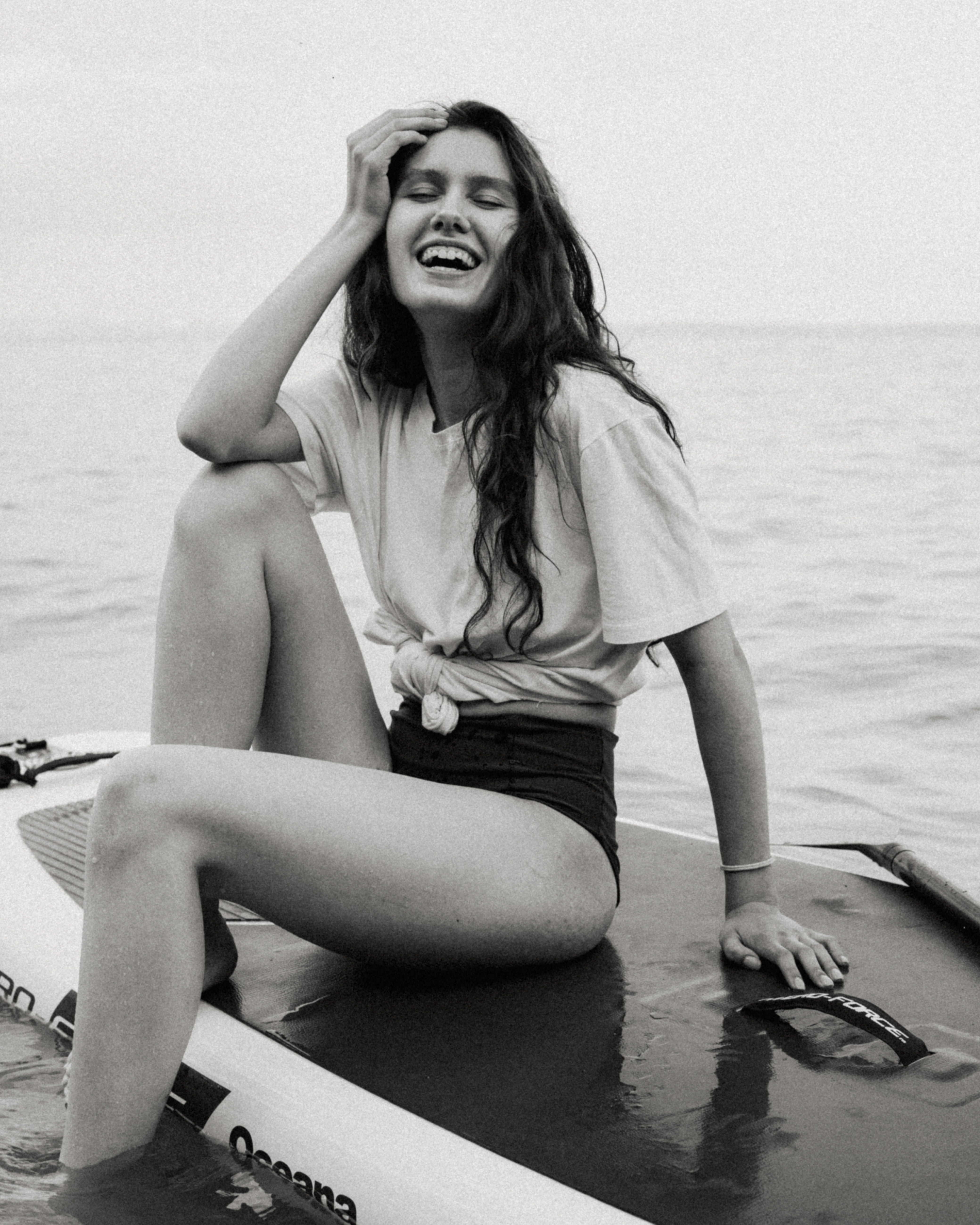 A woman laughing while sitting on a paddle board. | Source: Pexels