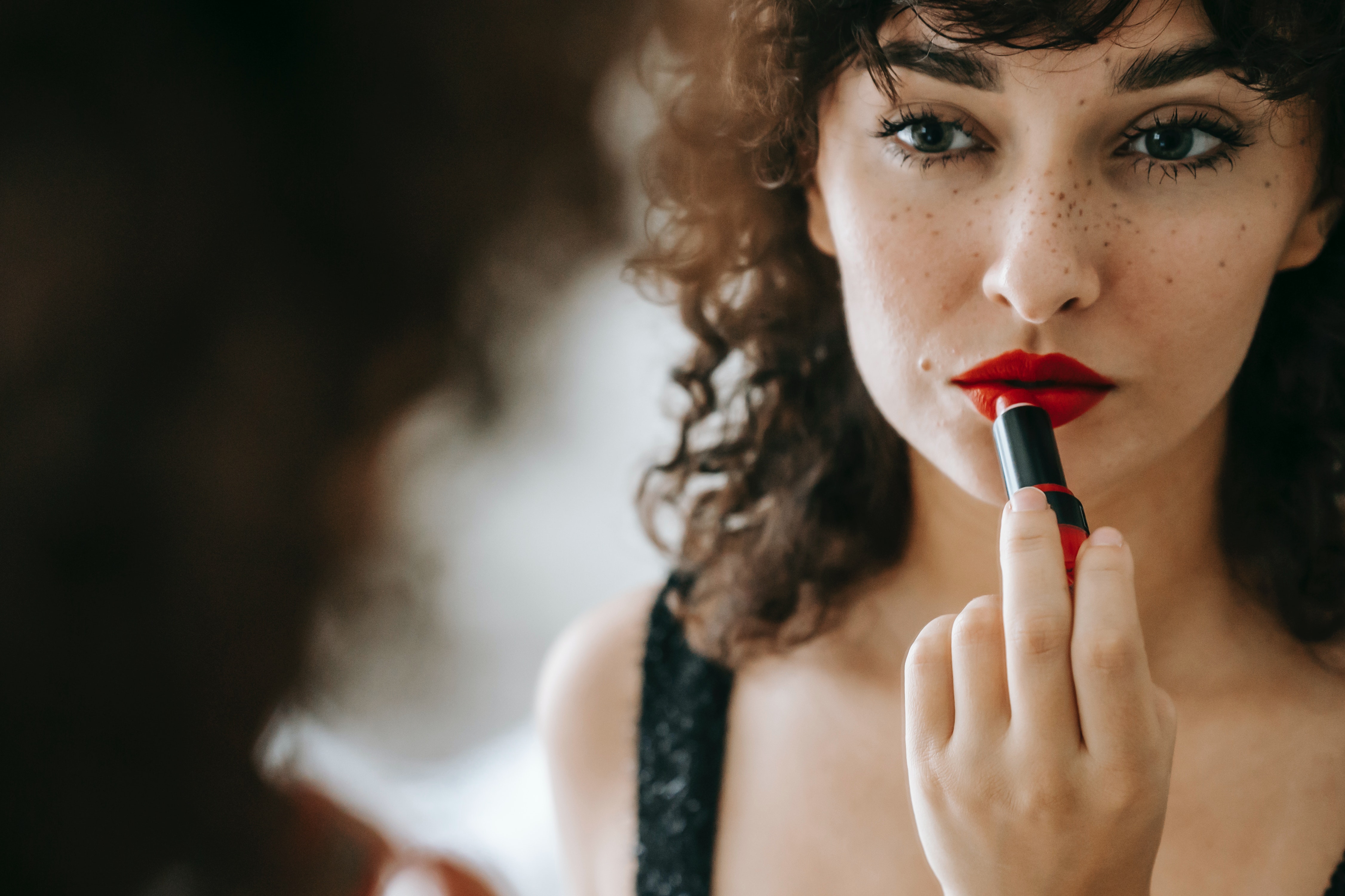A woman applying lipstick on in the mirror.  │Source: Pexels