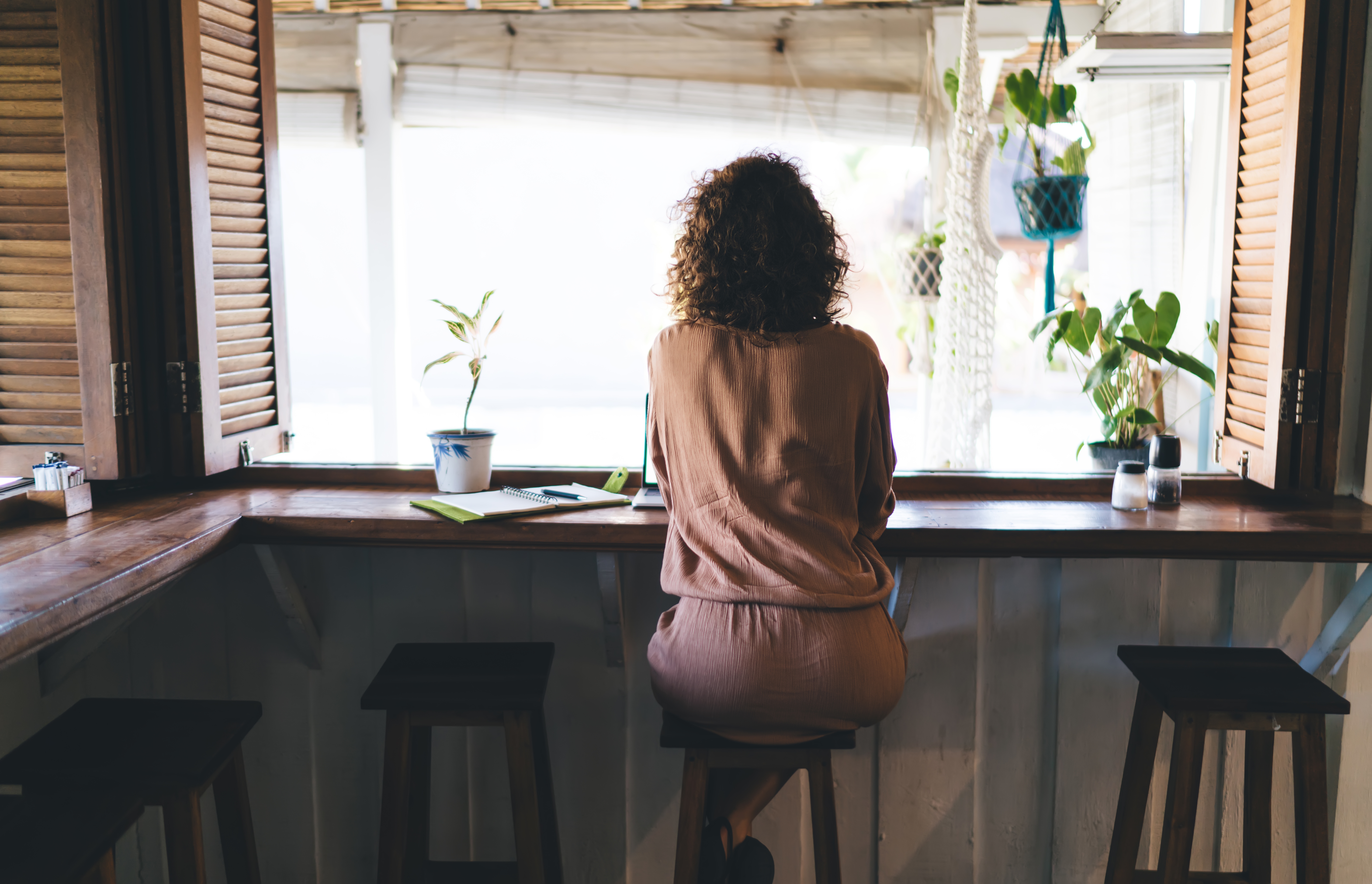 Vista trasera de una mujer sentada en la mesa del bar de una cafetería. | Fuente: Shutterstock