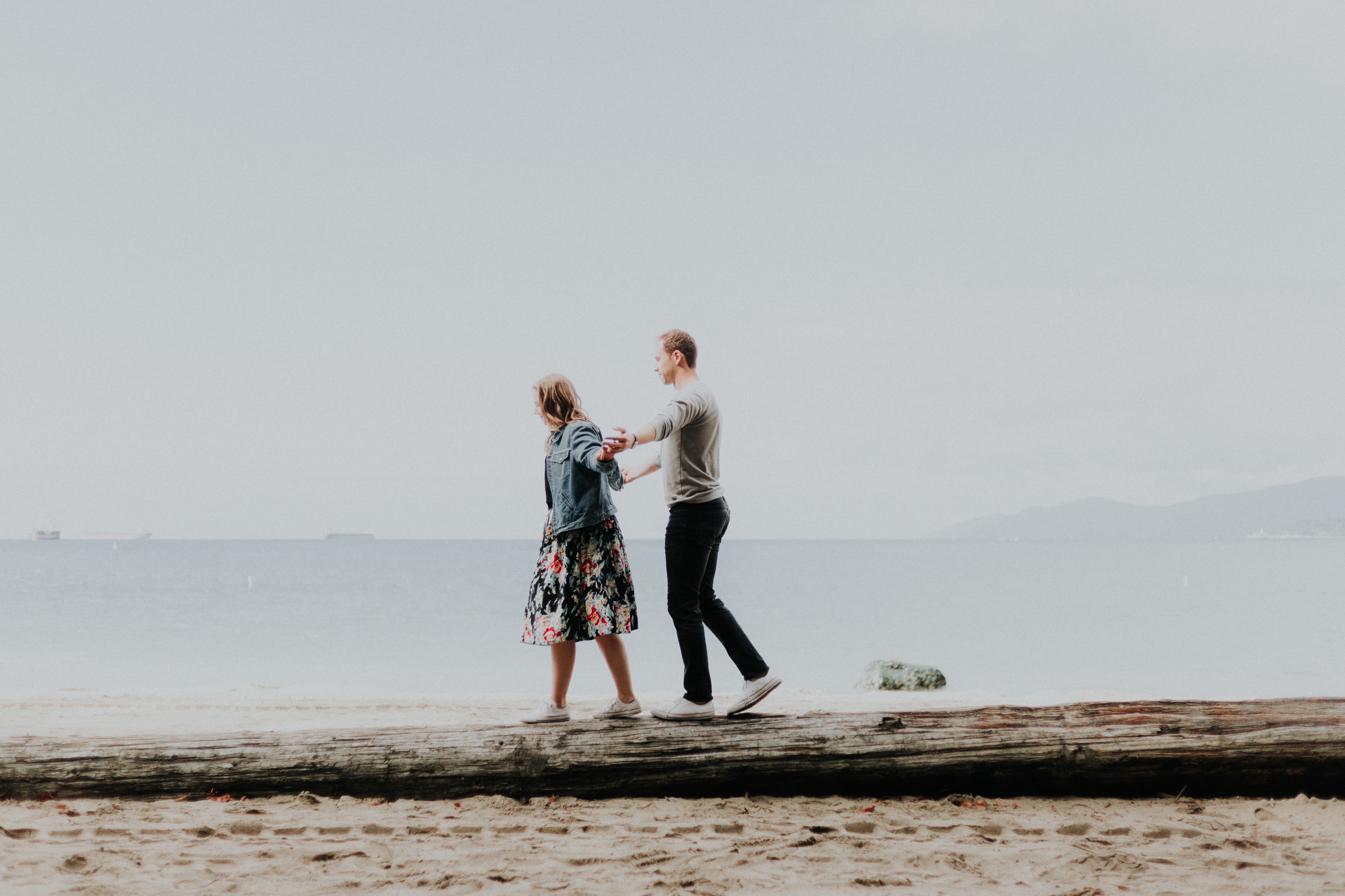 A couple balancing on a log in front of the ocean. | Source: Unsplash
