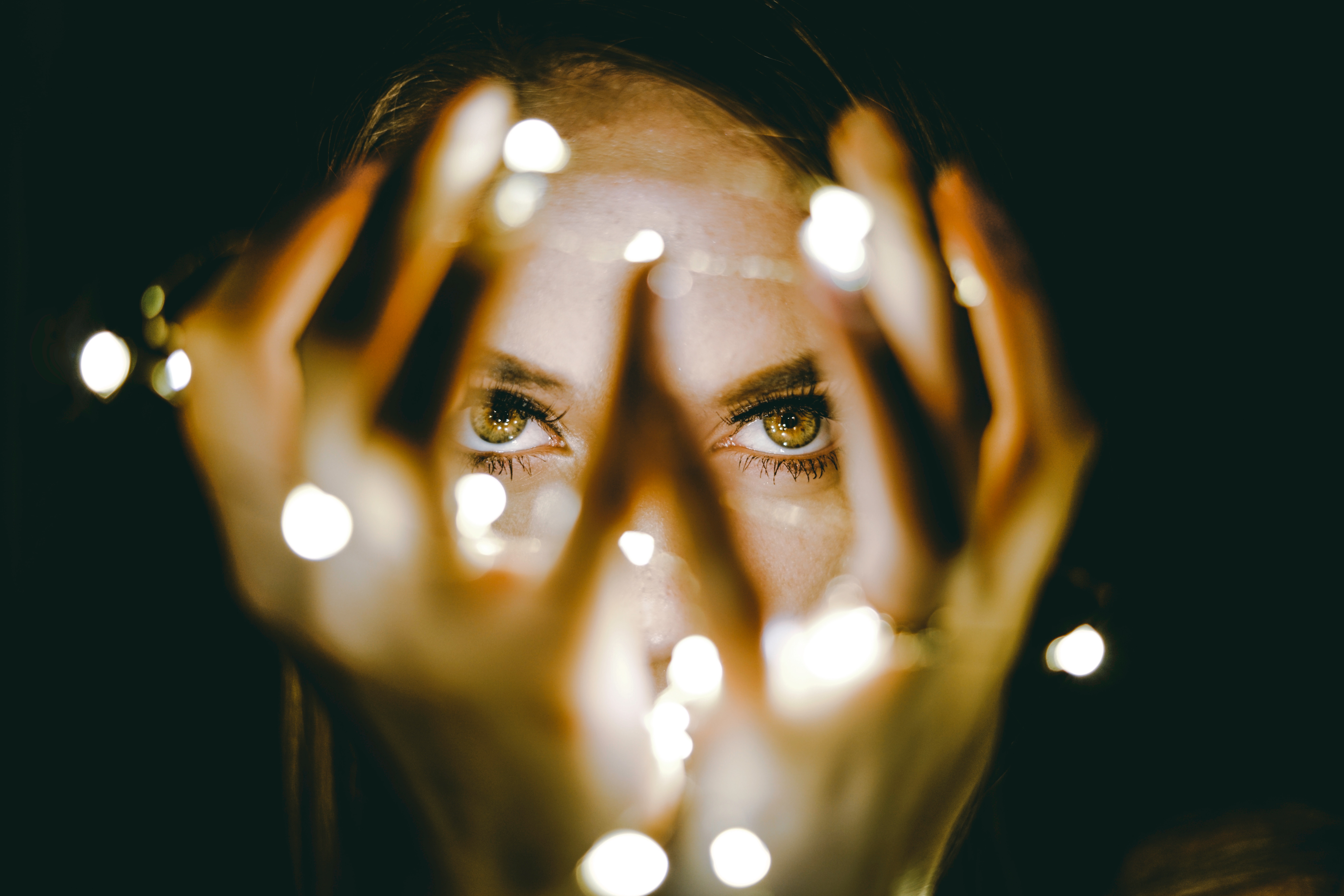 A woman looking through her fingers while holding string lights. | Source: Unsplash