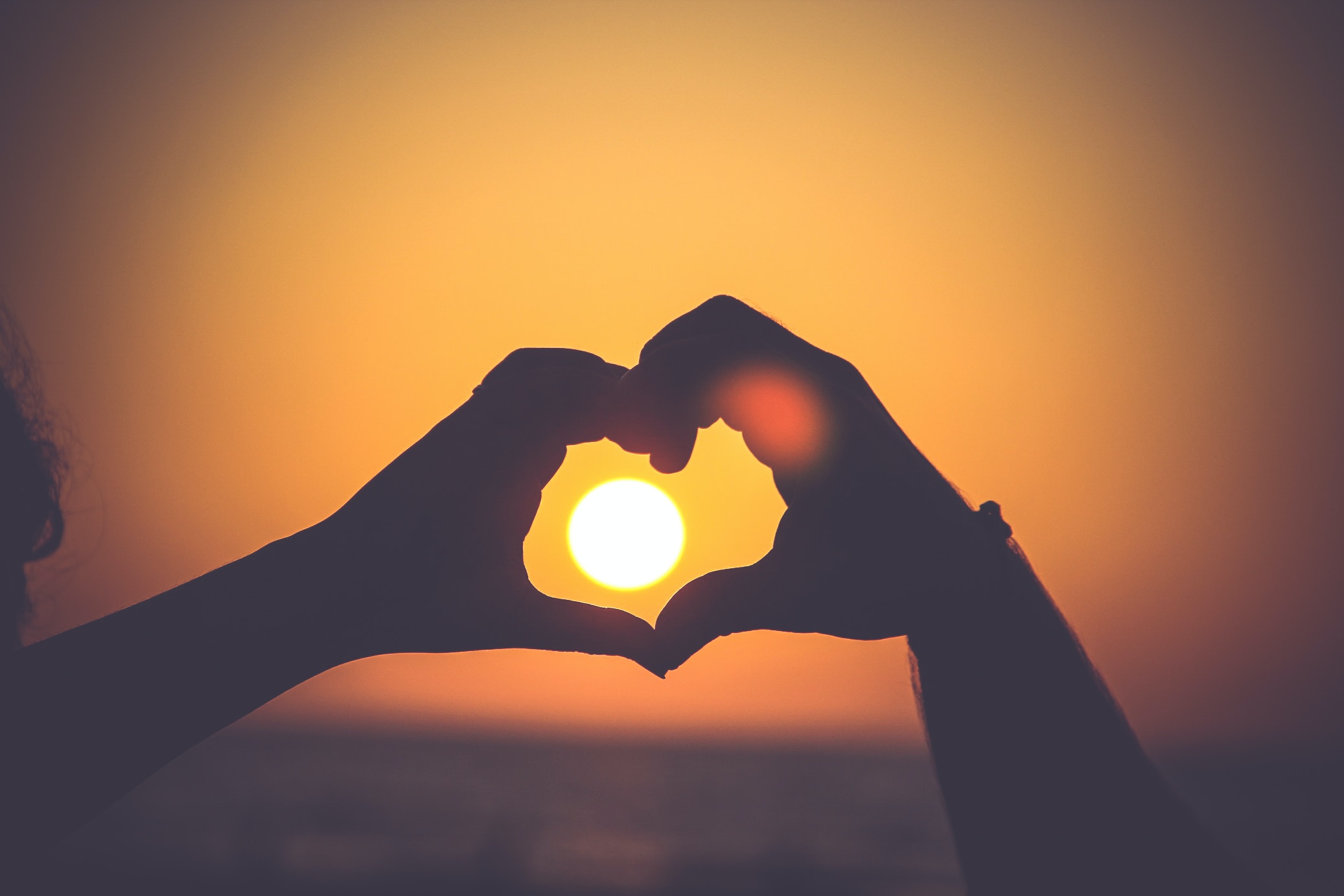 A photo of a person's hands forming a heart around the sun | Source: Unsplash