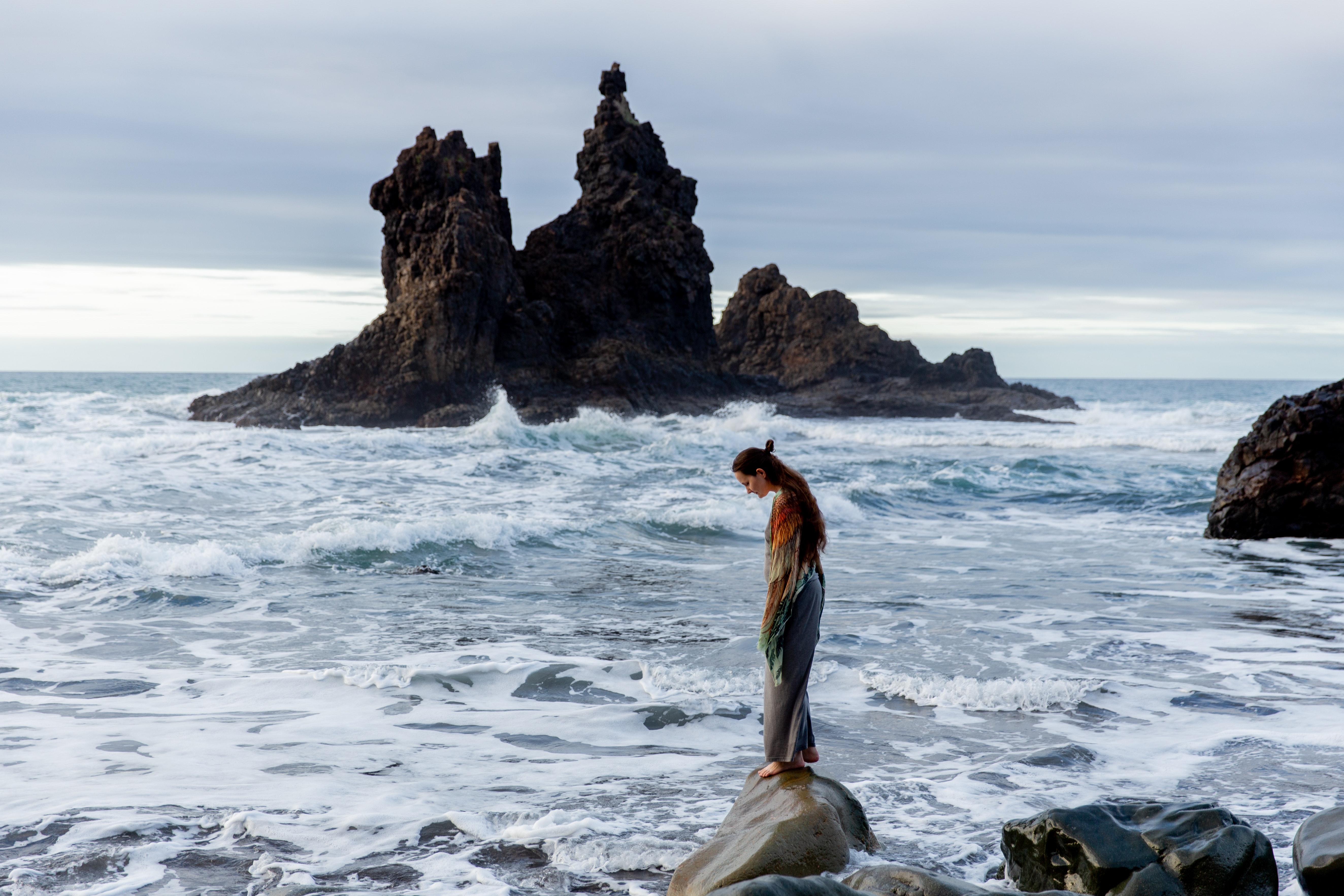 A woman standing on a rock in the ocean.│Source: Pexels