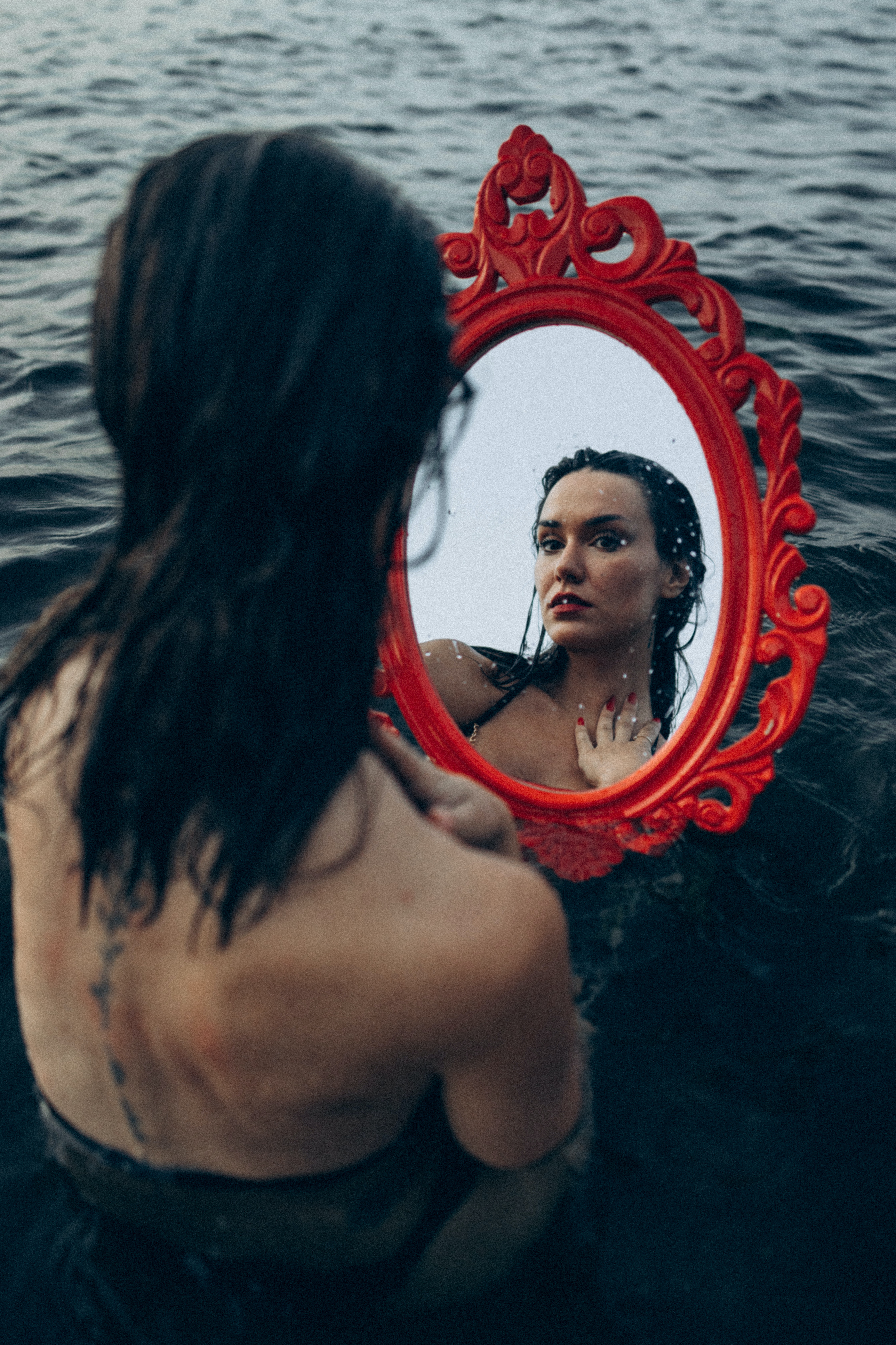 A woman looking at her reflection in a mirror while simultaneously in the ocean. | Source: Pexels