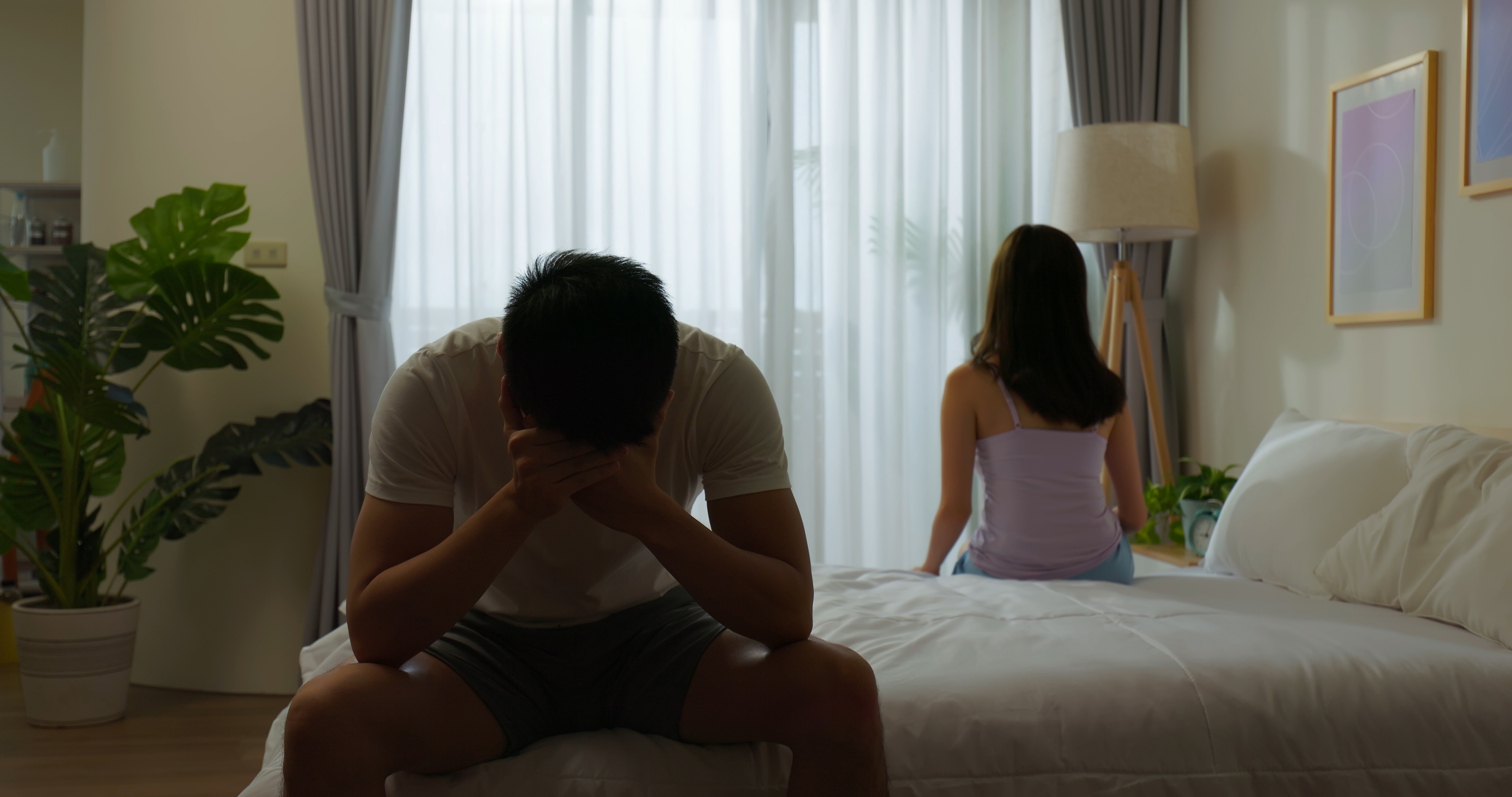 A couple sitting on their bed with their backs to each other | Source: Shutterstock