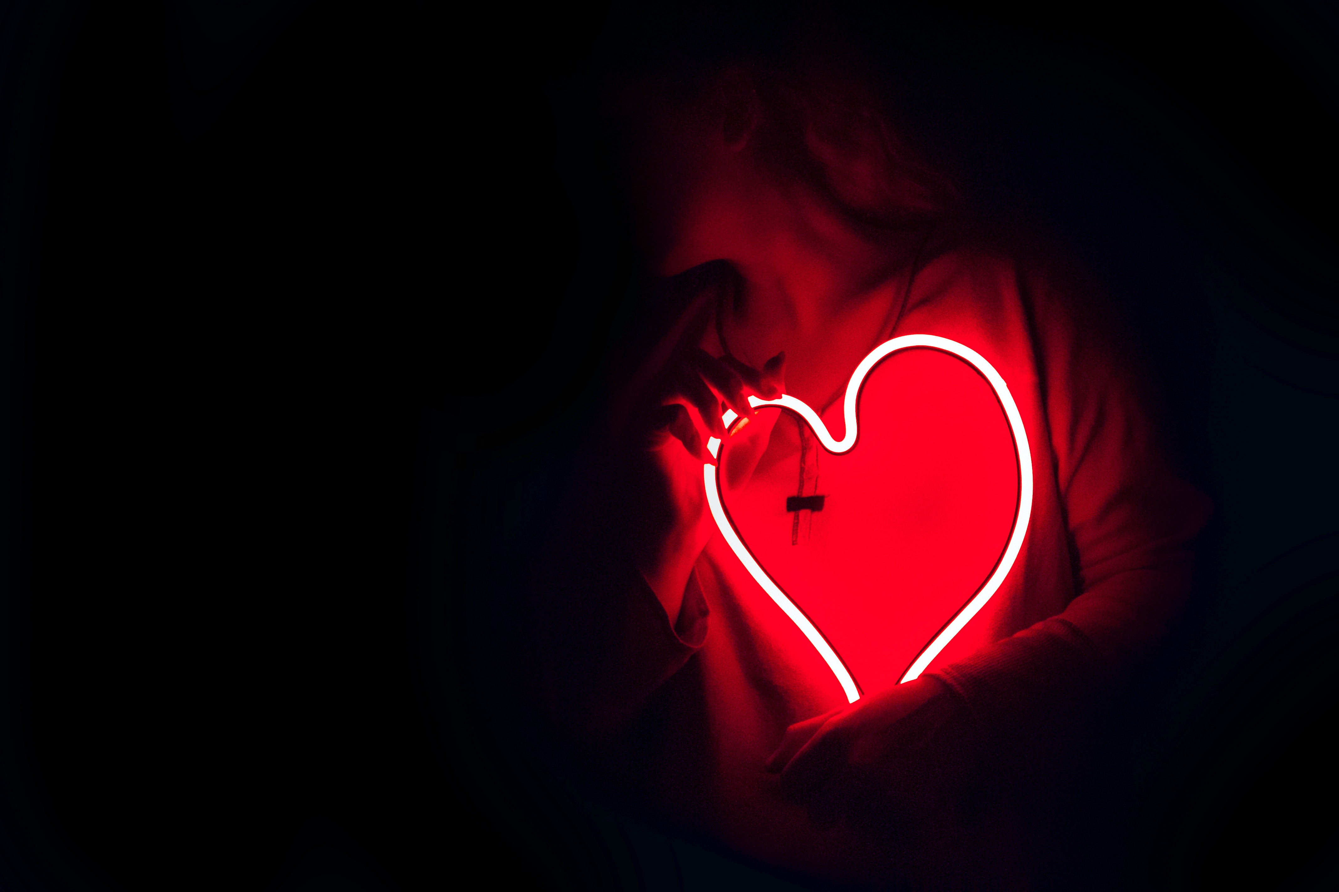 An individual holding a neon heart.┃Source: Unsplash