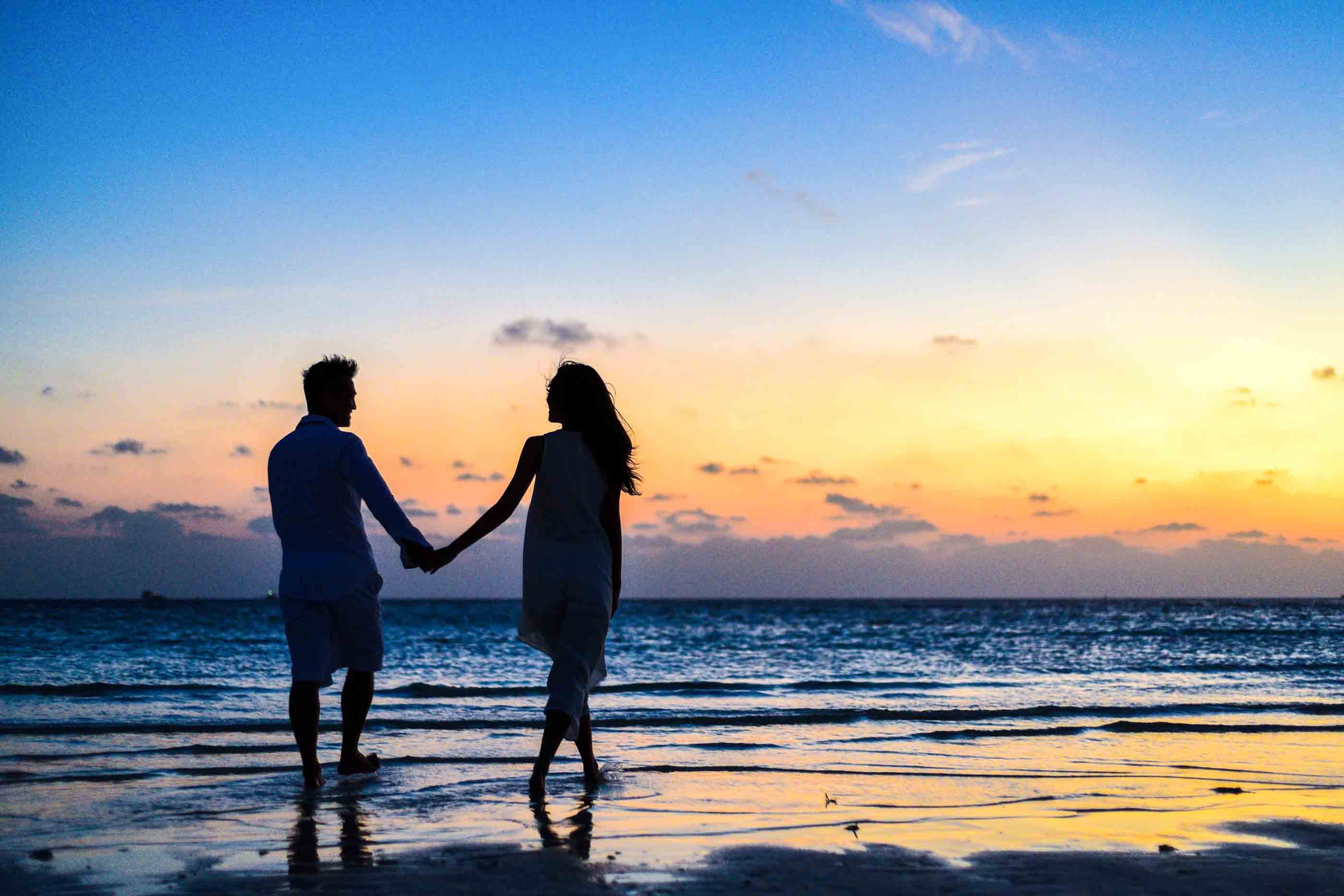 A couple holds hands while strolling at the beach.