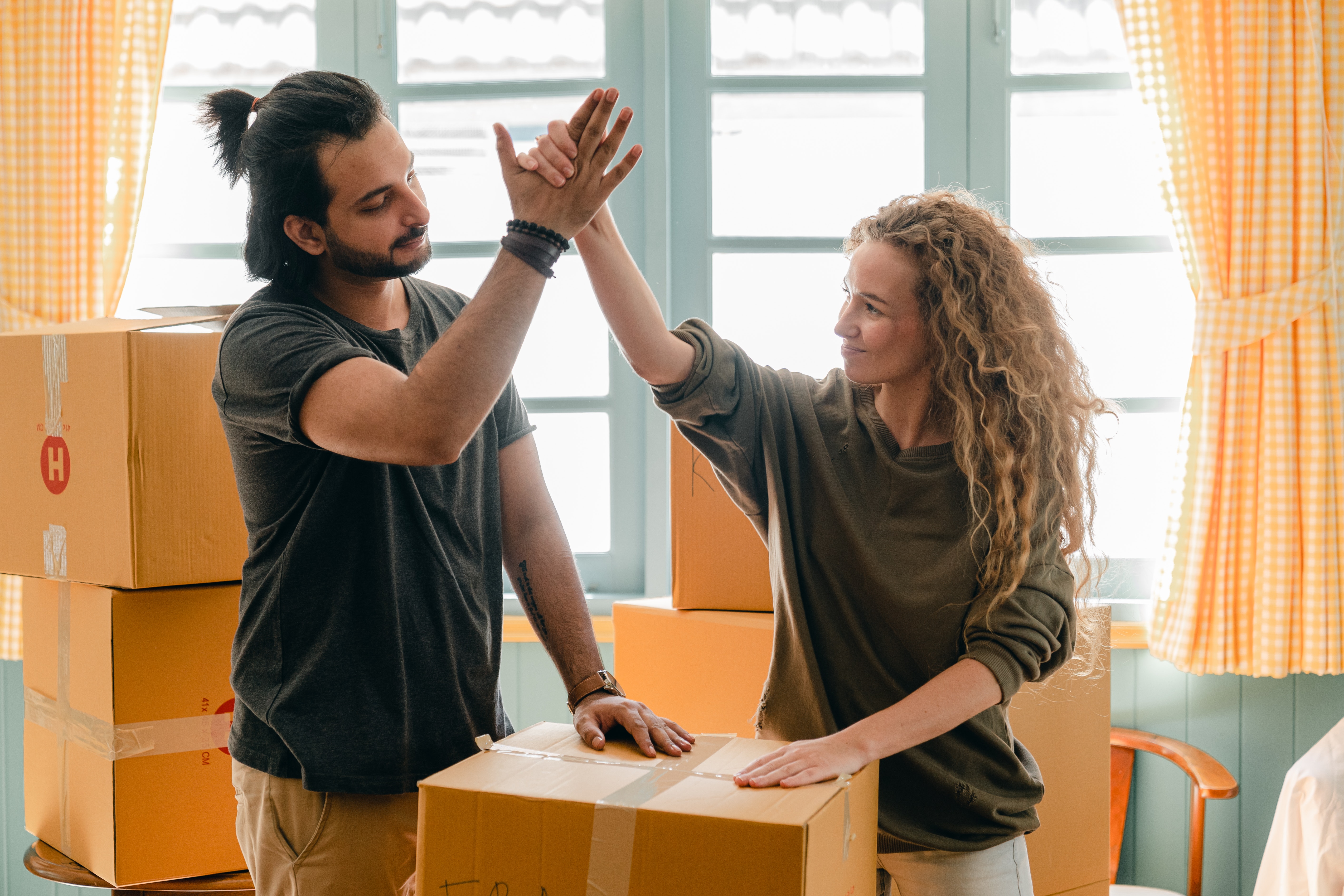 Multiracial couple giving high give standing near pile of boxes. | Source: Pexels