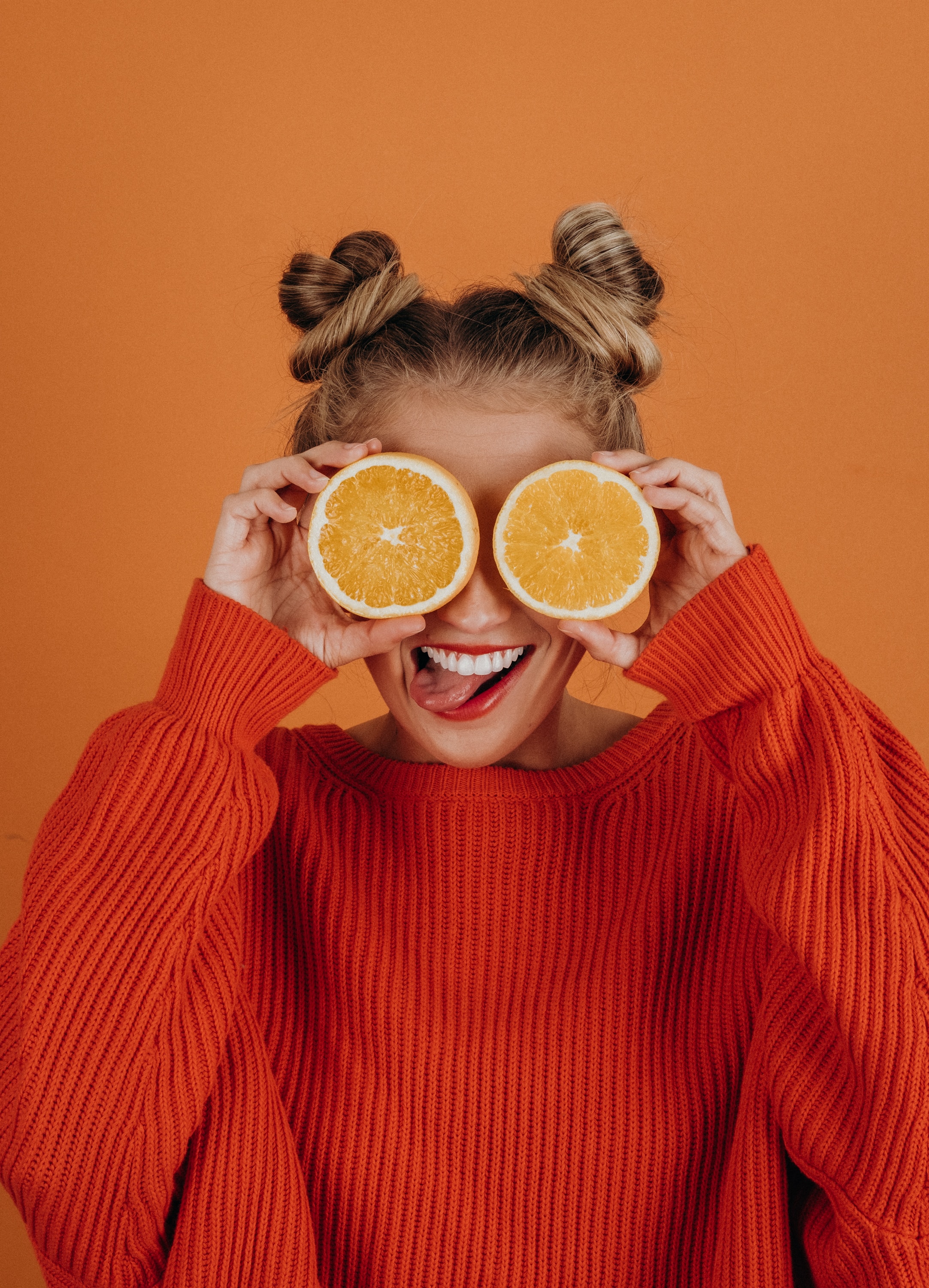A woman holding orange slices in front of her eyes. │Source: Unsplash