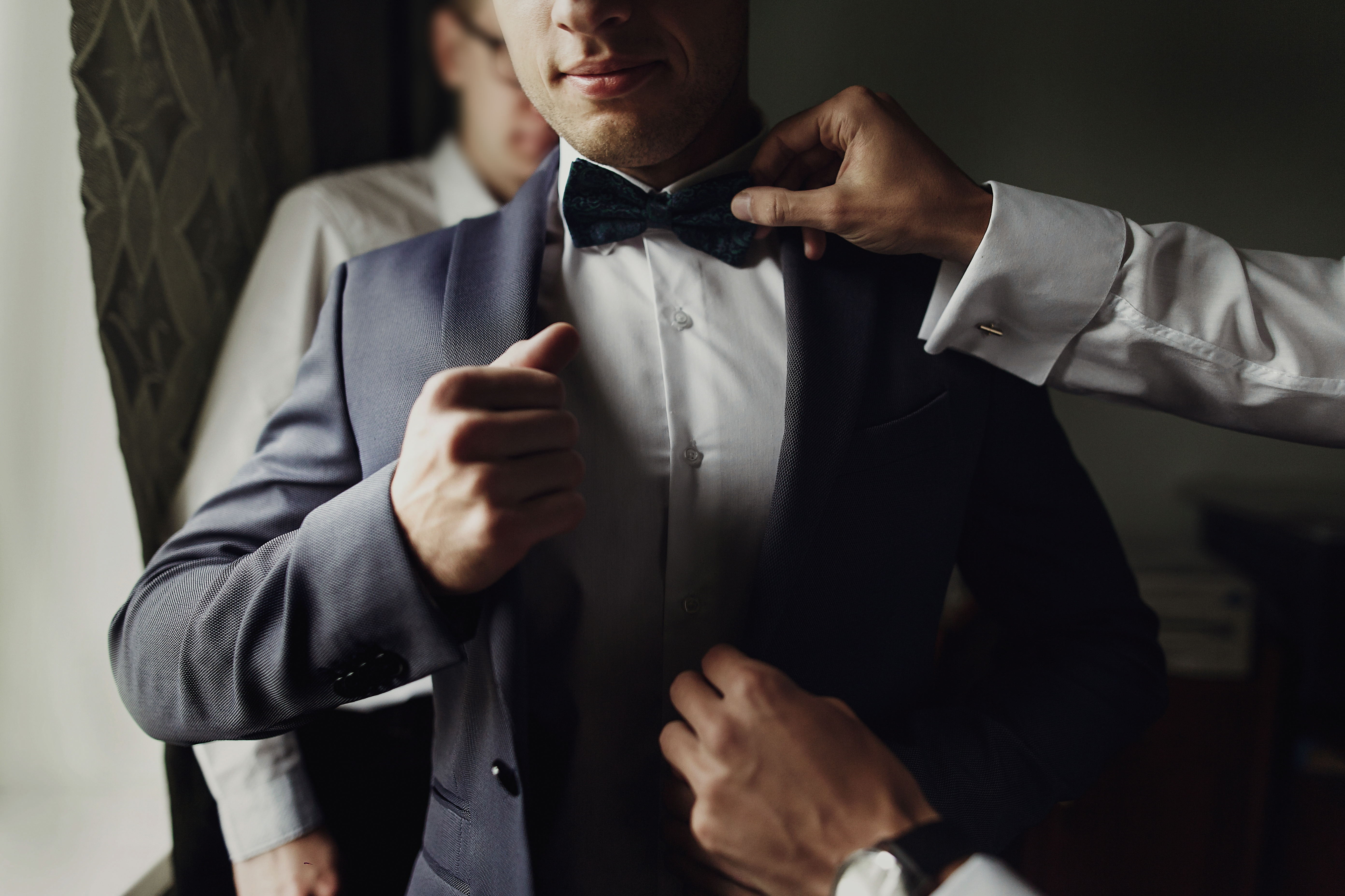 Estilosos padrinos de boda ayudando al feliz novio a prepararse por la mañana para la ceremonia nupcial. | Fuente: Shutterstock