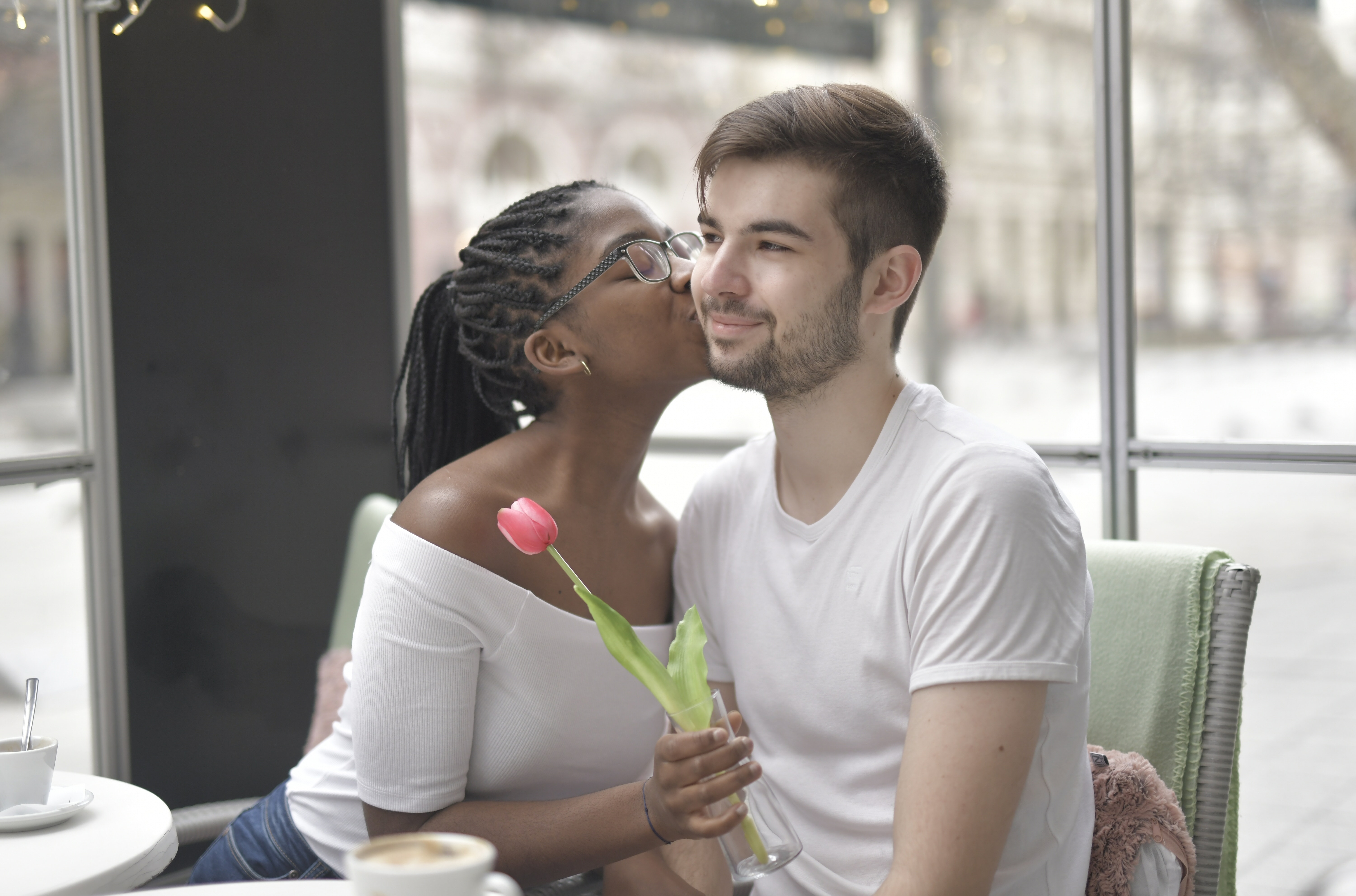 A woman kissing a man's cheek while holding a flower. | Source: Pexels