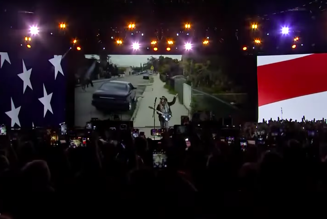 Billy Ray Cyrus trying to hype the crowd up with gestures after the first technical mishap with his guitar. | Source: YouTube/PBS NewsHour