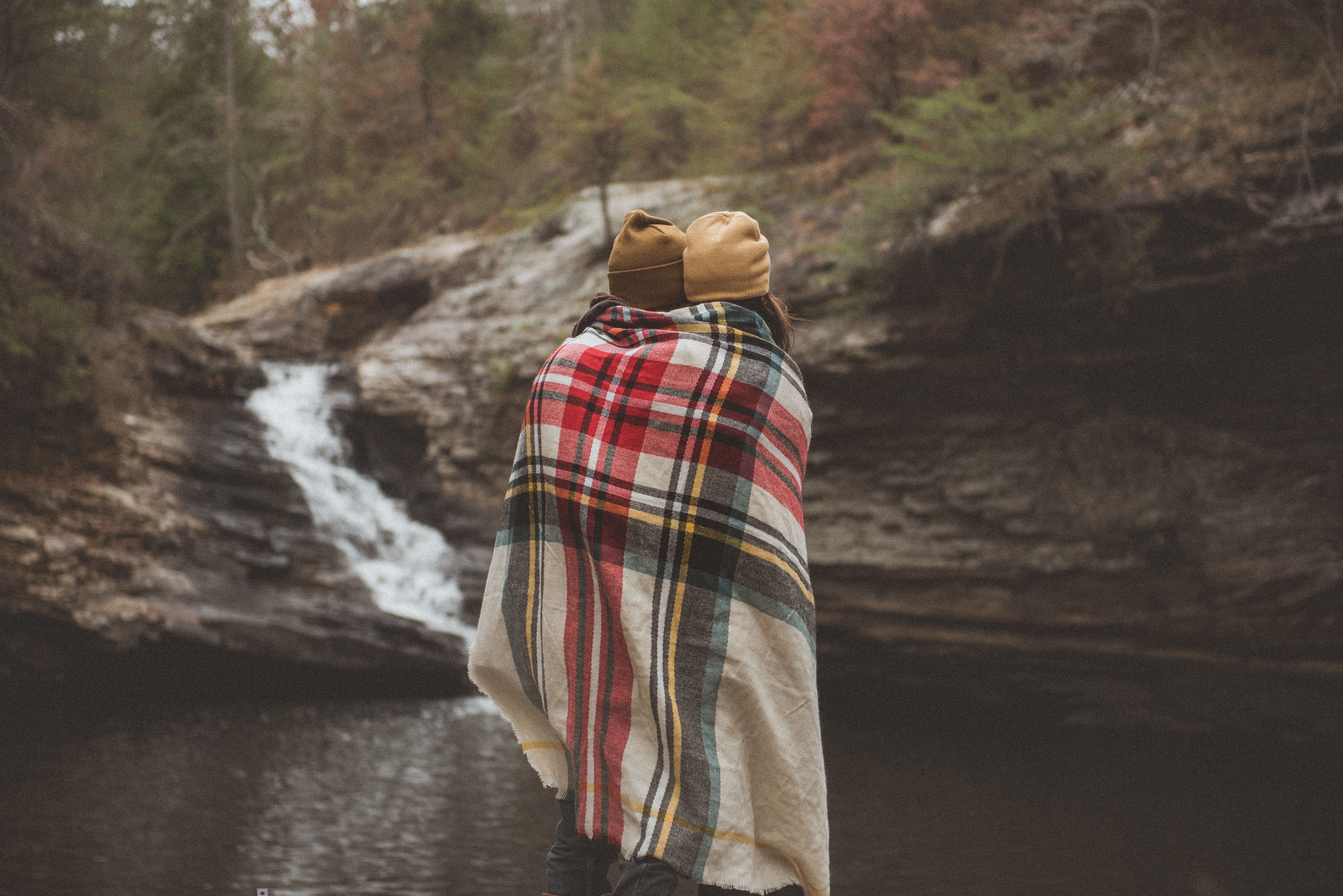 A couple with a blanket wrapped around them in front of a body of water. | Source: Unsplash