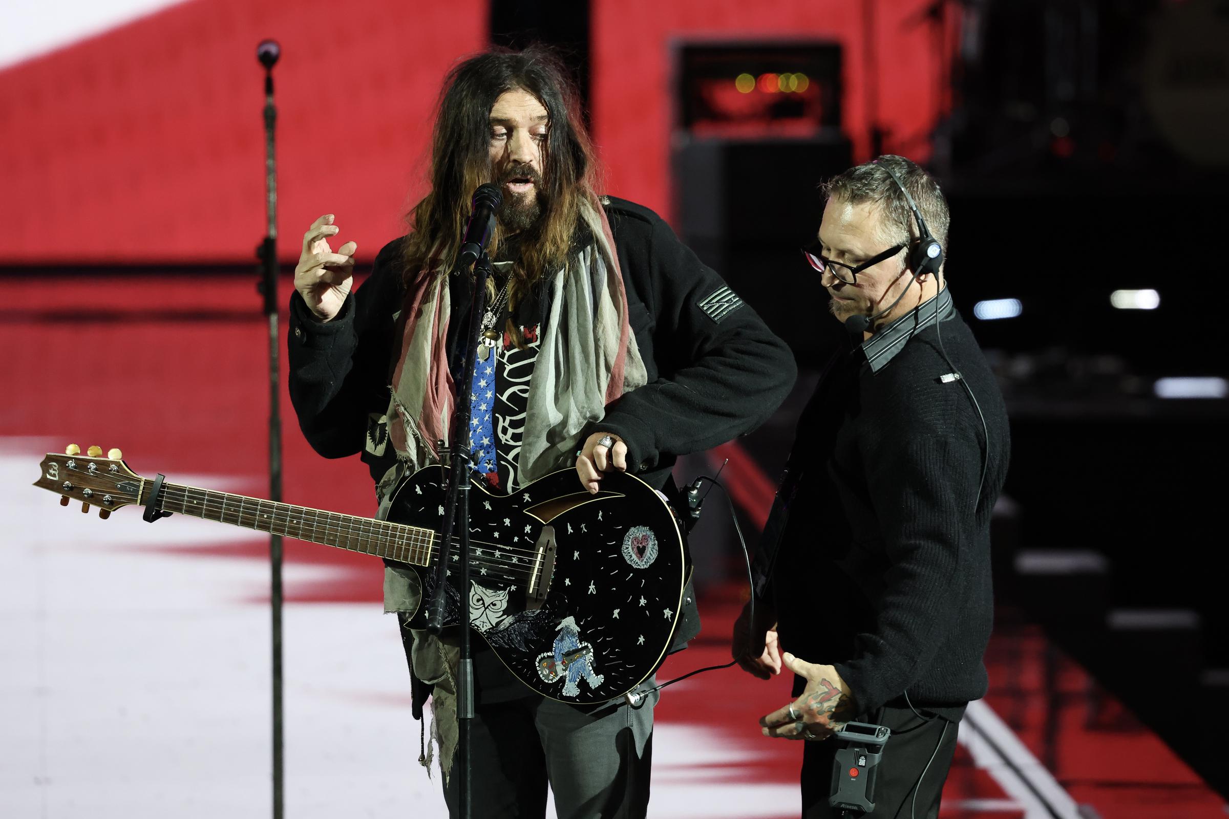 A technician attempting to help Billy Ray Cyrus with his guitar. | Source: Getty Images