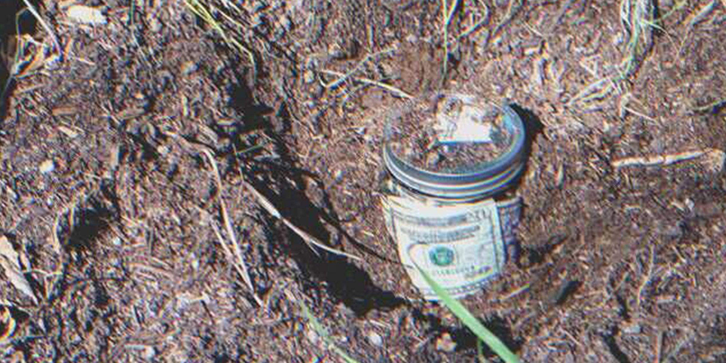 Money stashed in a glass jar buried on the ground | Source: Shutterstock