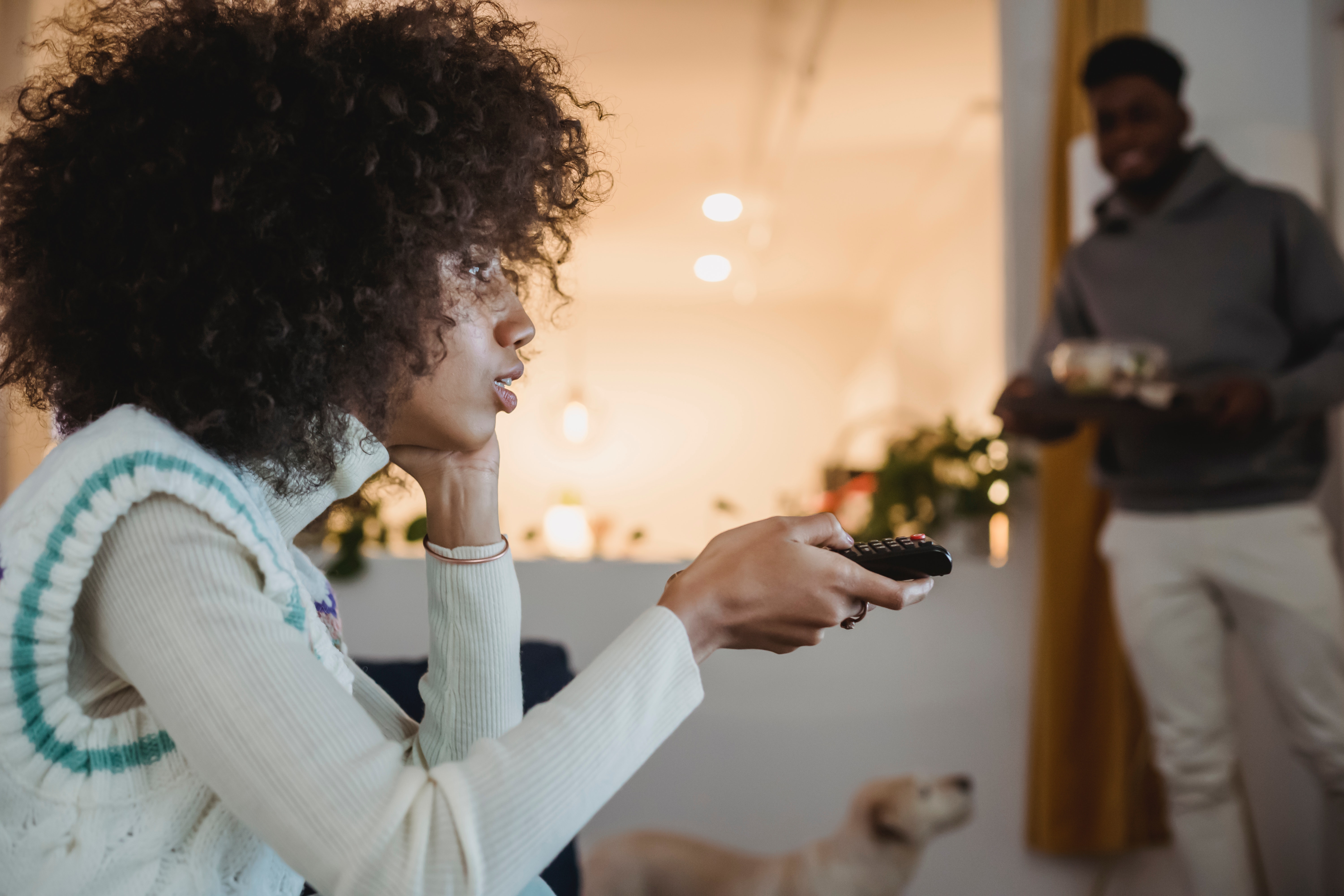 Young Black Woman Watching TV With Interest Near Boyfriend Standing In Room. | Source: Pexels