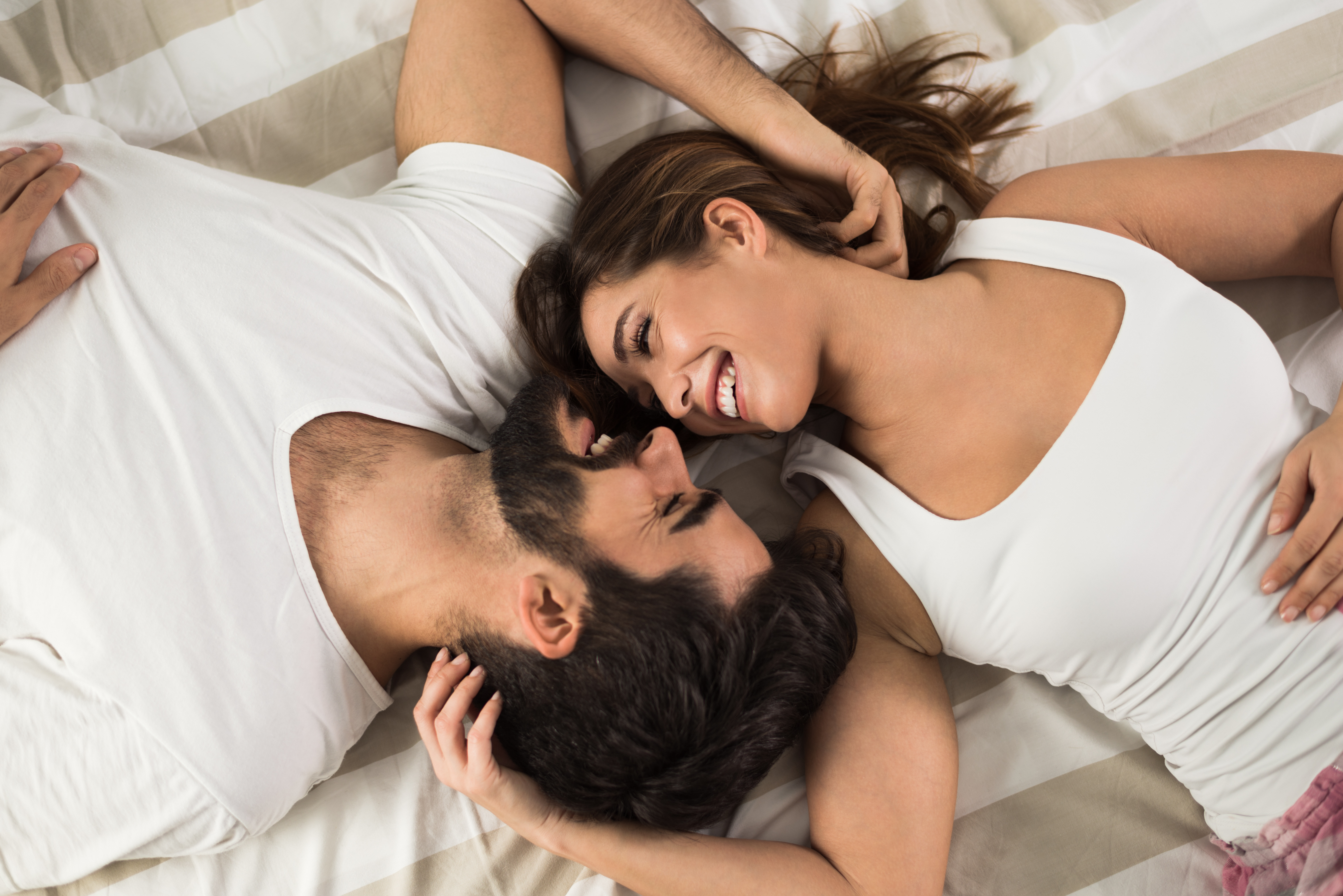 A happy couple laying in bed while smiling at each other | Source: Shutterstock