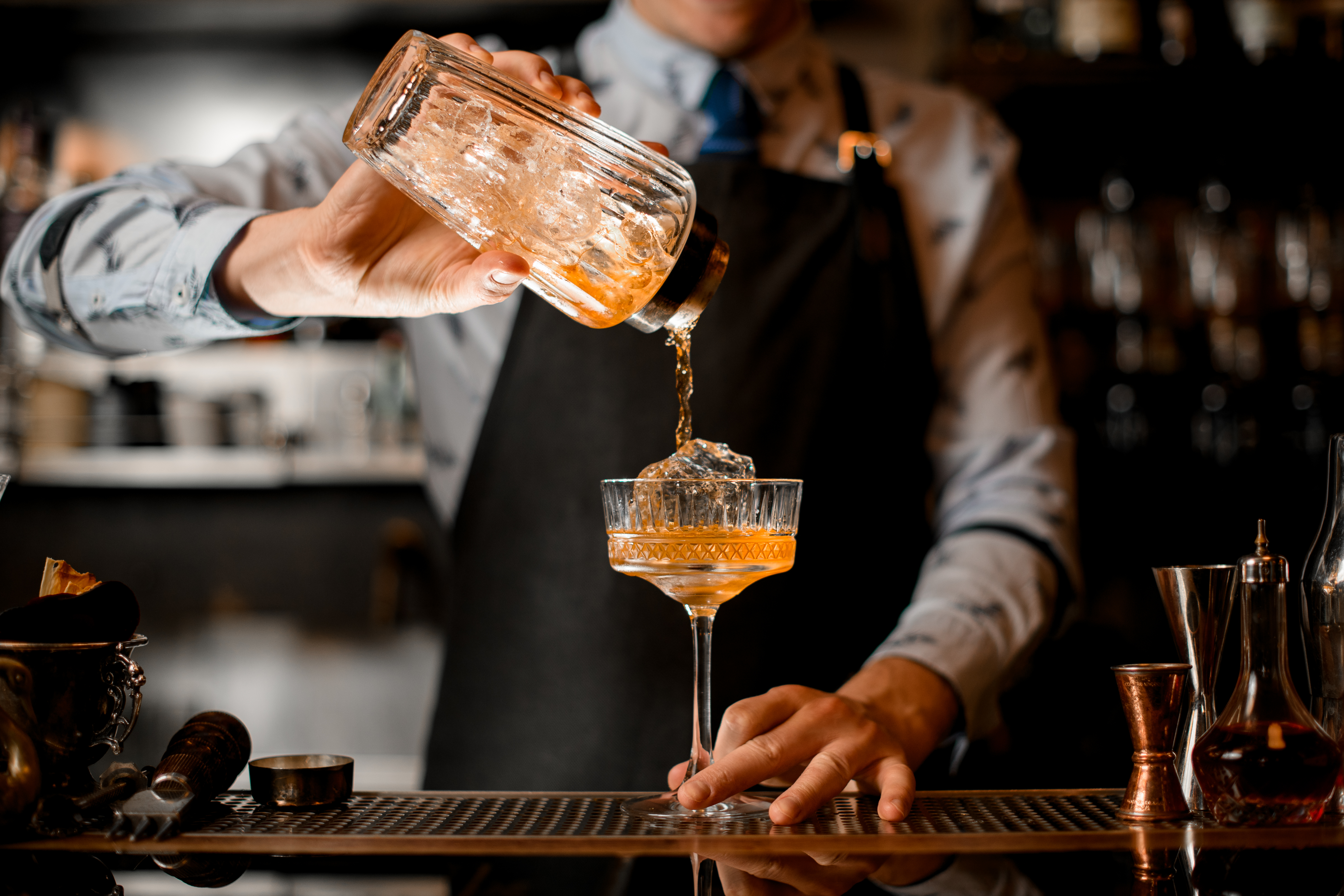 El camarero vierte suavemente el cóctel terminado de la coctelera en el vaso. | Fuente: Shutterstock